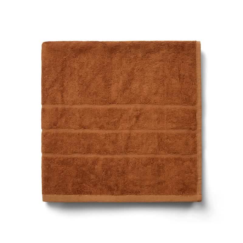 Bambooya Bambus badehåndklæde (70 x 140 cm) i en rustfarve, fremstillet af økologisk bomuld og med tre vandrette syninger, er pænt foldet i en firkantet form og vist på en hvid baggrund.