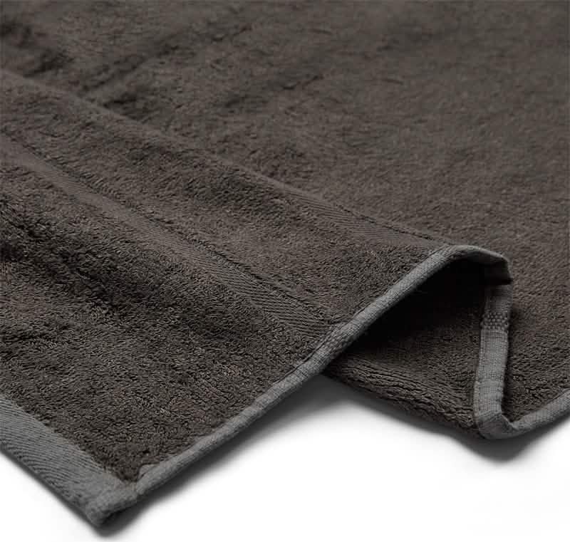 Et nærbillede af Bambooya Bambus badelagen (90 x 180 cm) i mørkegrå, med et foldet hjørne, der fremhæver det bløde, strukturerede stof og de pænt afsluttede kanter.