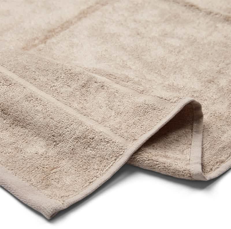 Et nærbillede af Bambooya Bambus badelagen (90 x 180 cm) i beige med en struktureret overflade og et pænt foldet hjørne fremhæver det bløde og absorberende økologiske bomuldsstof.
