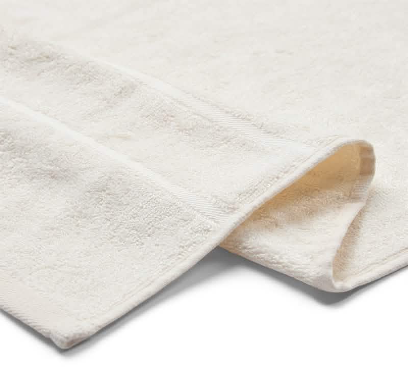 Et nærbillede af Bambooya Bambus badelagen (90 x 180 cm) i off-white viser det bløde, absorberende stof og det diskrete kantdesign. Den er fremstillet af økologisk bomuld, er OEKO-TECH Standard 100-certificeret og vises på en almindelig hvid baggrund.